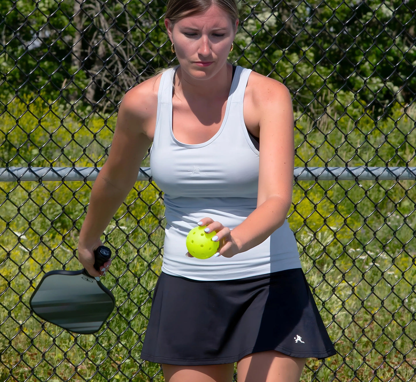 Woman wearing a Grey tank top holding a paddle and ball on a pickleball court Gris