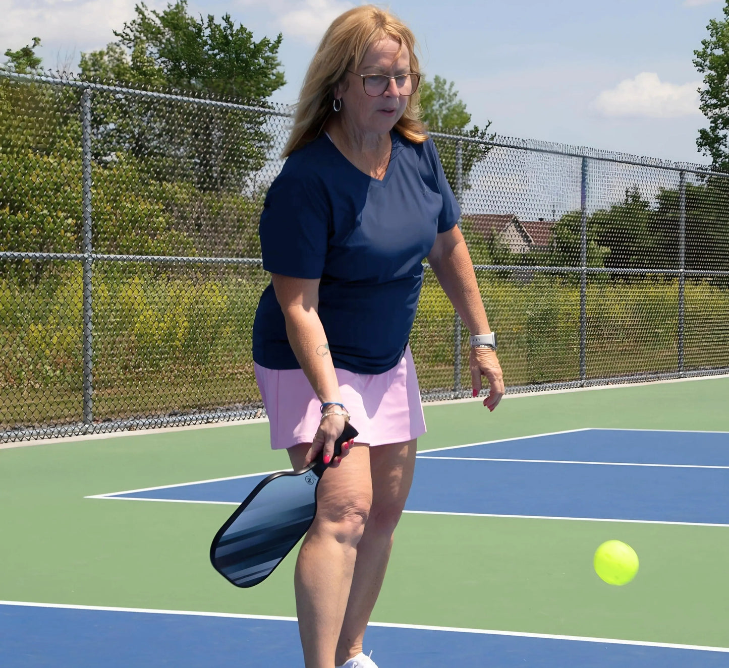 Woman wearing a Blue t-shirt playing pickleball on an outdoor court with a ball and paddle Bleu