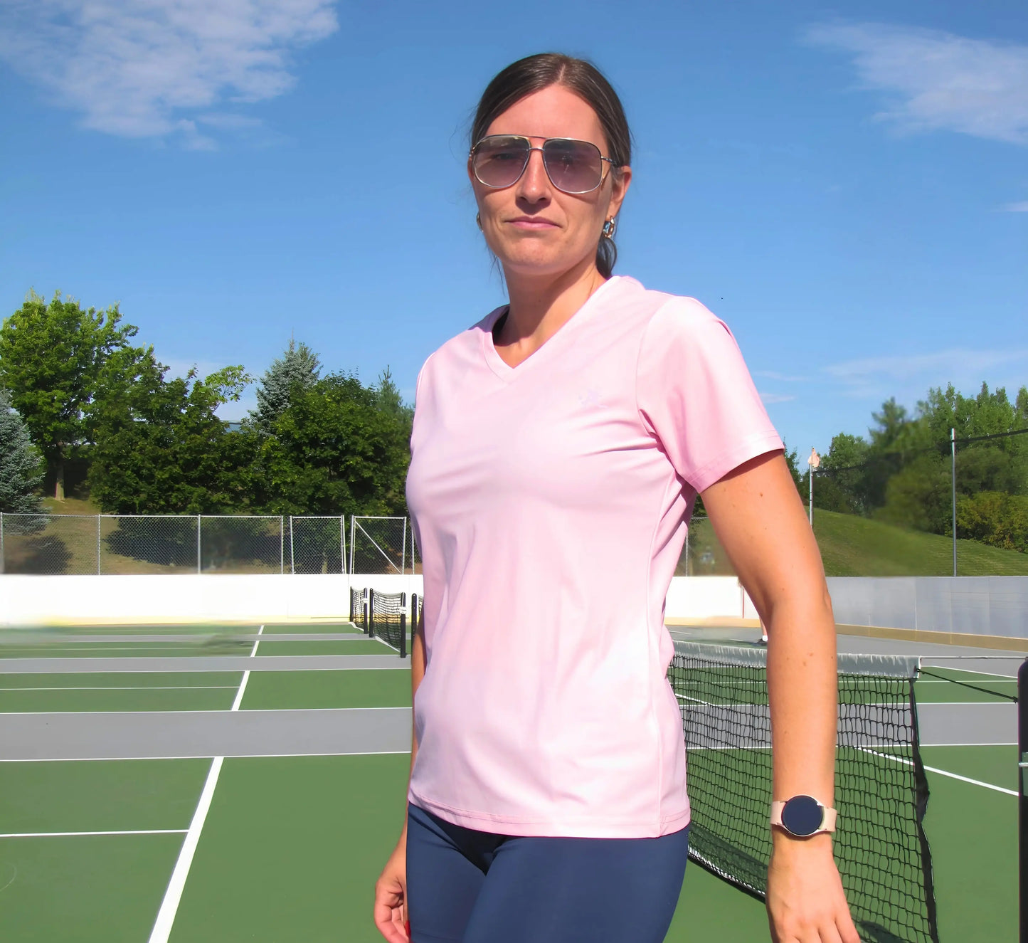 Woman standing on a pickleball court wearing a Pink t-shirt and sunglasses Rose