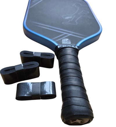 A pickleball paddle with a black textured face, blue edge trim, and a black wrapped overgrip, shown alongside three black overgrip tapes rolls on a plain white background.
