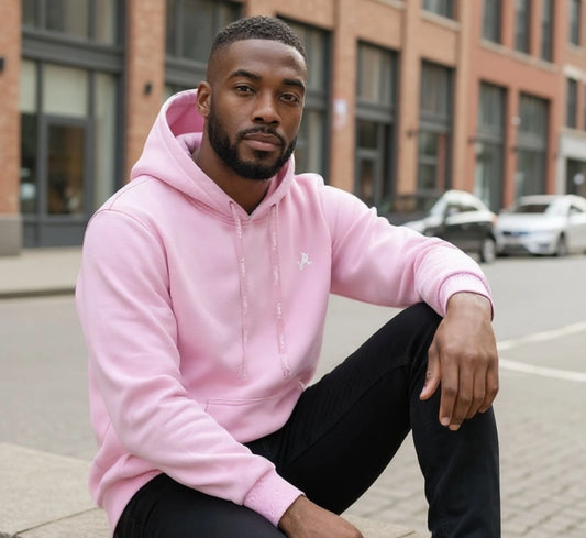 Man wearing a pink hoodie sitting on a street corner with a building in the background