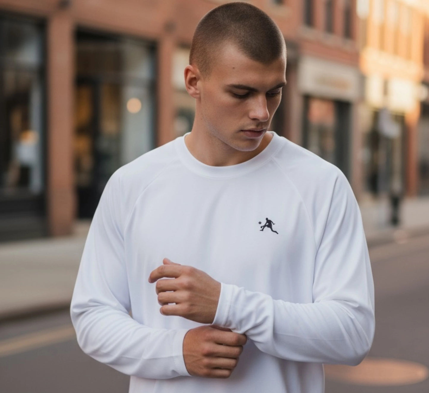 Man wearing a white long-sleeve shirt with a small black logo on a city street.