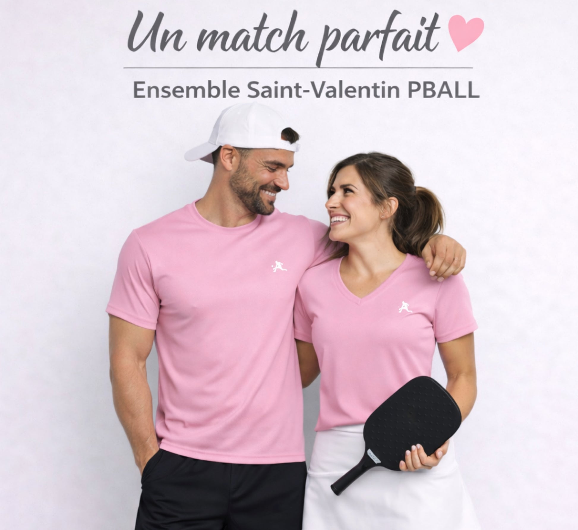 Couple wearing pink shirts with a pickleball paddle, standing against a light background.
