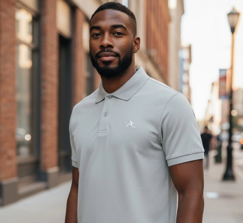 Man wearing a light gray polo shirt with a logo on a city street