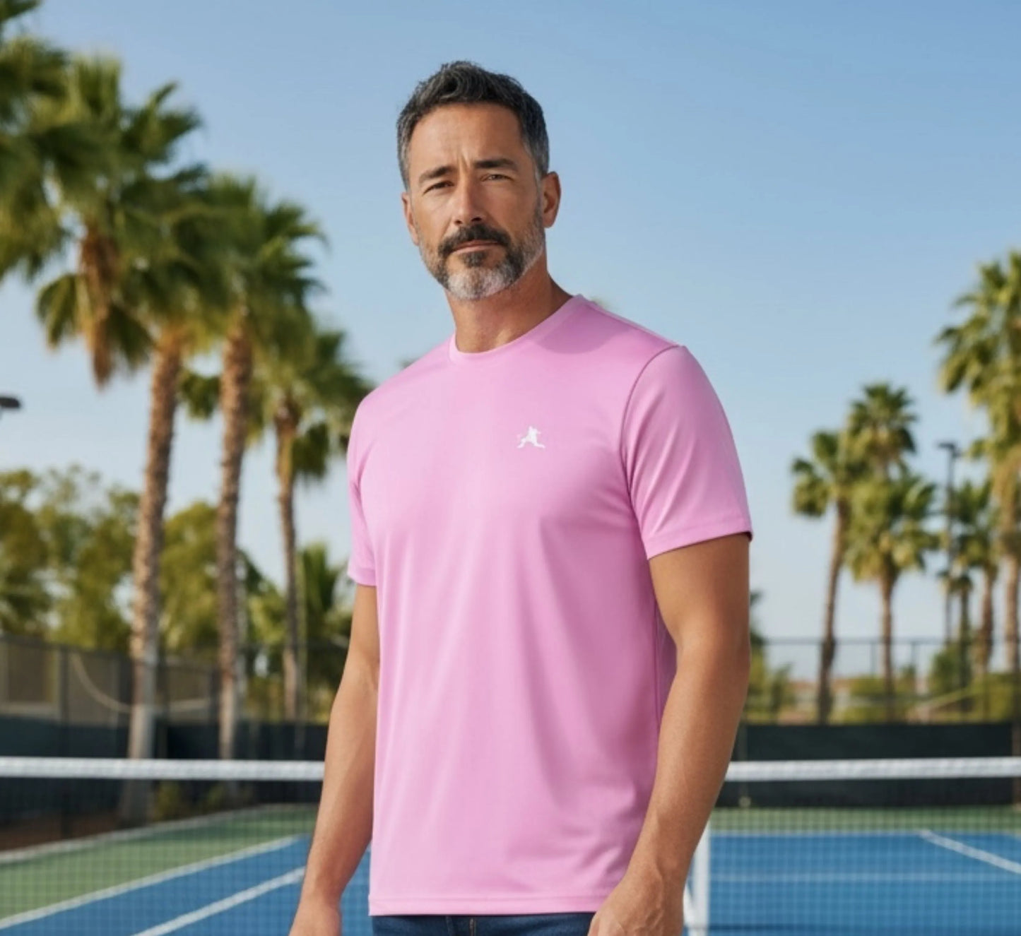 Man wearing a pink shirt on a pickleball court with palm trees in the background