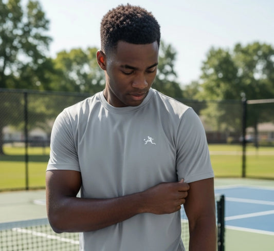 Man wearing a light gray t-shirt with a logo on a pickleball court