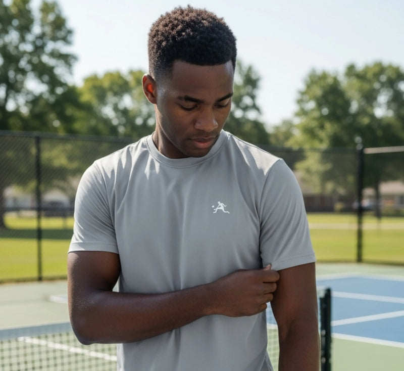 Man wearing a light gray t-shirt with a logo on a pickleball court