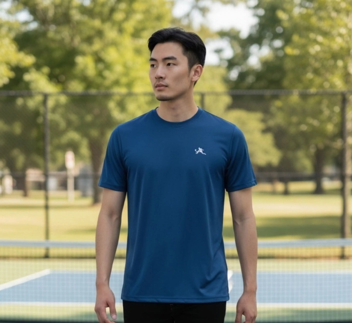 Man wearing a blue t-shirt on a pickleball court with trees in the background