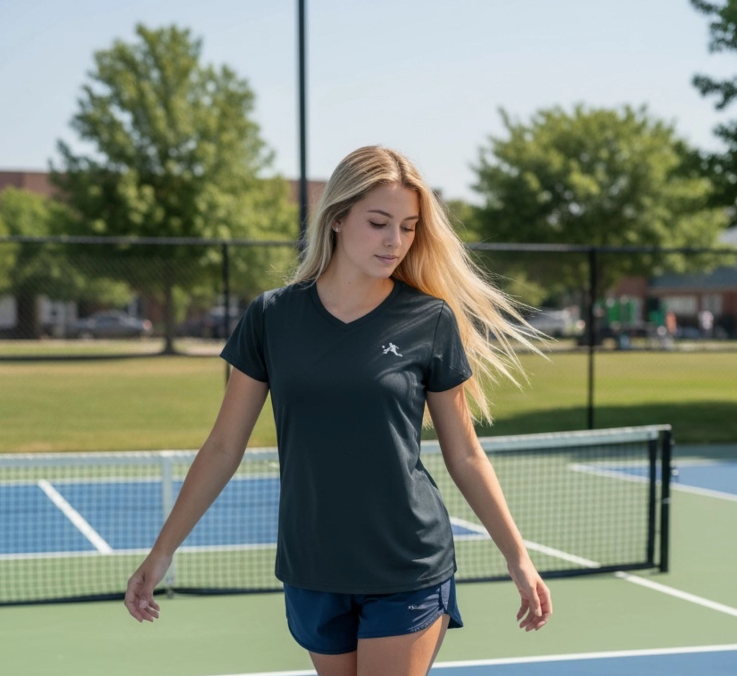 Woman on a pickleball court wearing a black t-shirt with a logo