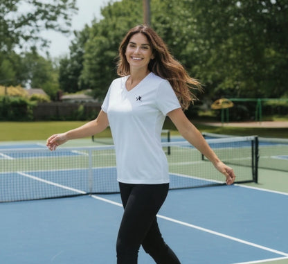 Woman standing on a pickleball court wearing a white t-shirt with a logo.