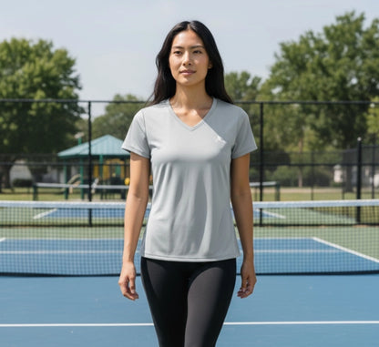 Woman standing on a pickleball court wearing a light gray t-shirt and dark leggings.