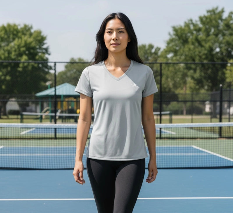 Woman standing on a pickleball court wearing a light gray t-shirt and dark leggings.