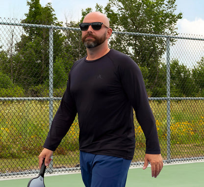 Man in Black long-sleeve shirt and blue shorts holding a pickleball paddle on a tennis court Noir