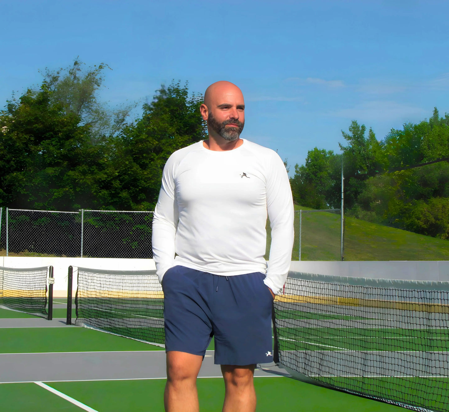 Man standing on a pickleball court wearing a White long-sleeve shirt and blue shorts Blanc