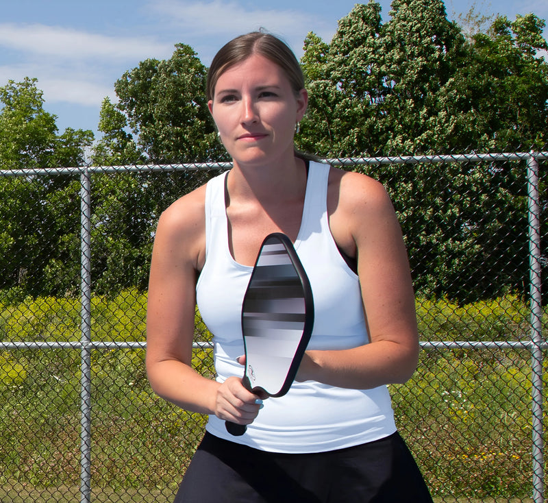 Femme en camisole Blanc tenant une raquette sur un terrain de pickleball avec des arbres en arrière-plan. White