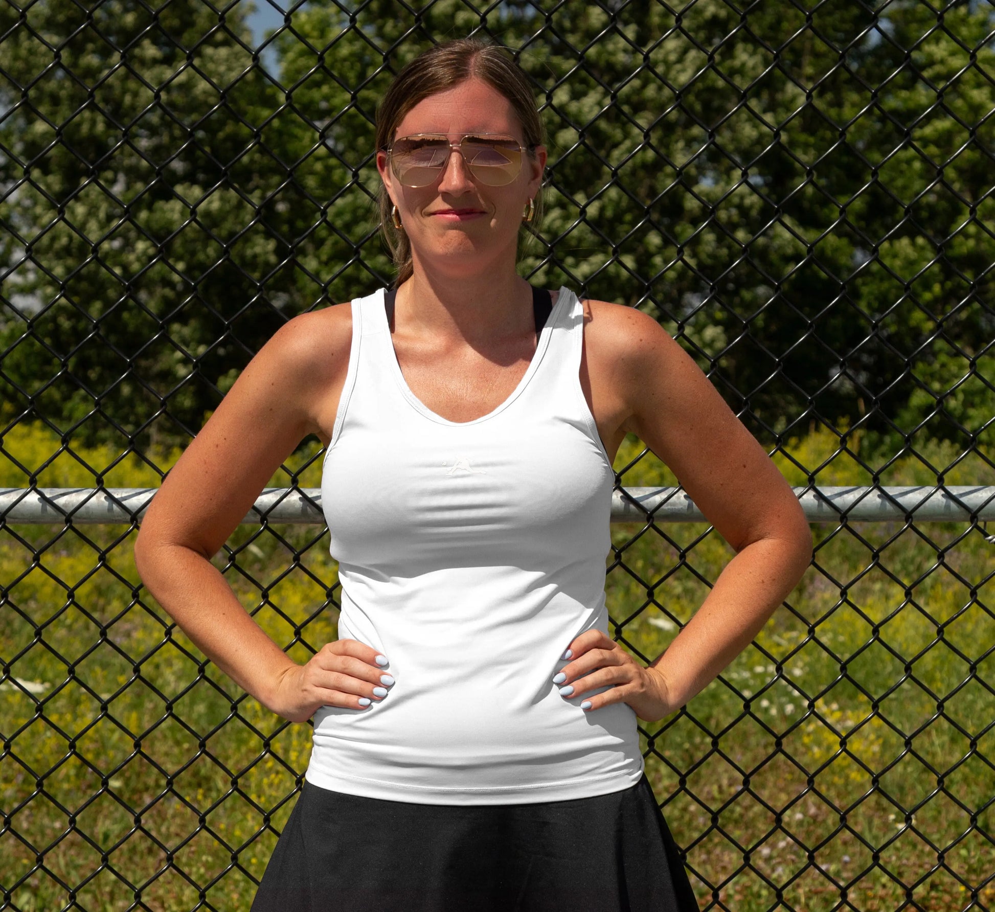 Femme portant une camisole Blanc et une jupe noire devant une clôture grillagée. White