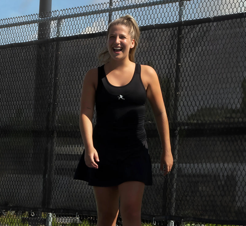 Femme en camisole Noir, debout sur un terrain de pickleball avec une clôture en arrière-plan. Black