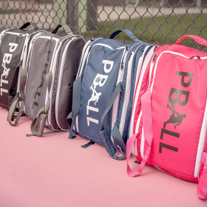 4 pickleball bags of different colours in front of a fence on a court