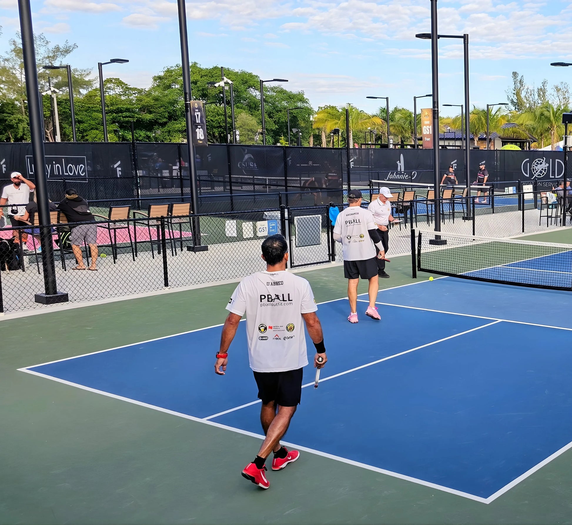 People playing pickleball on an outdoor court with a fence and trees in the background.