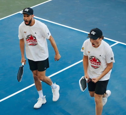 Two pickleball players on a court wearing Canada-themed shirts and hats.
