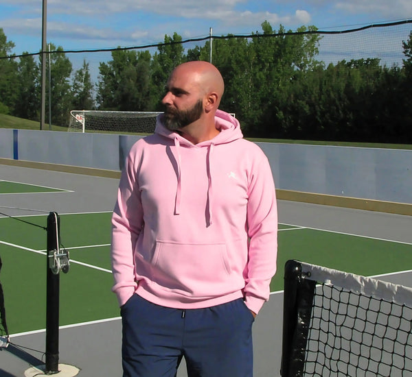 Man in a Pink hoodie standing on a pickleball court with trees in the background Rose