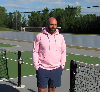 Man in a Pink hoodie standing on a pickleball court with trees in the background Rose