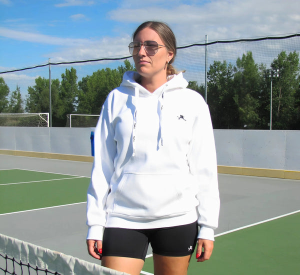 Woman in a White hoodie and black shorts standing on a pickleball court Blanc