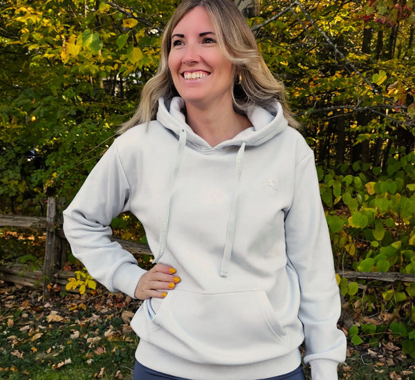 Woman wearing a light grey hoodie outdoors with greenery in the background