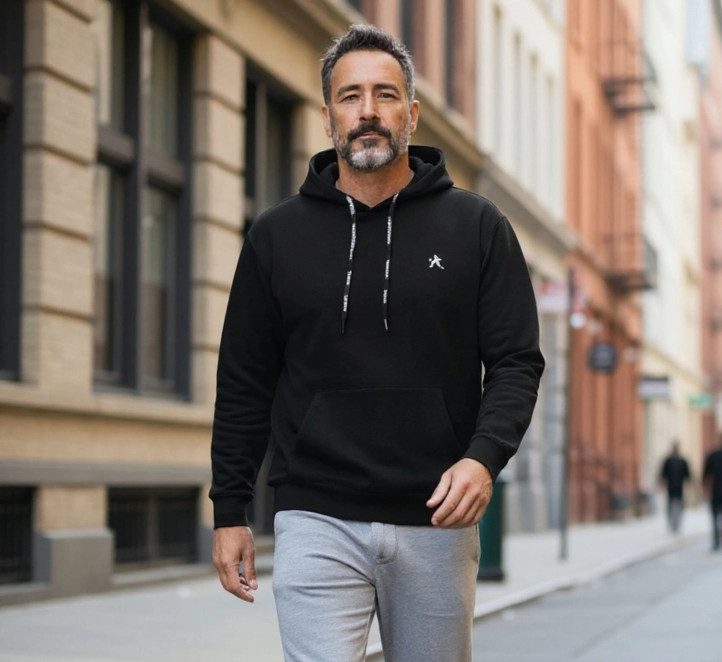 Man wearing a black hoodie with a logo on a city street