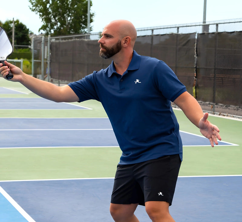 Homme en polo Bleu et short noir sur un terrain de pickleball. Blue