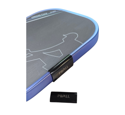 A close-up of a rectangular pickleball paddle weight and a black plastic clip labeled PBALL. 
