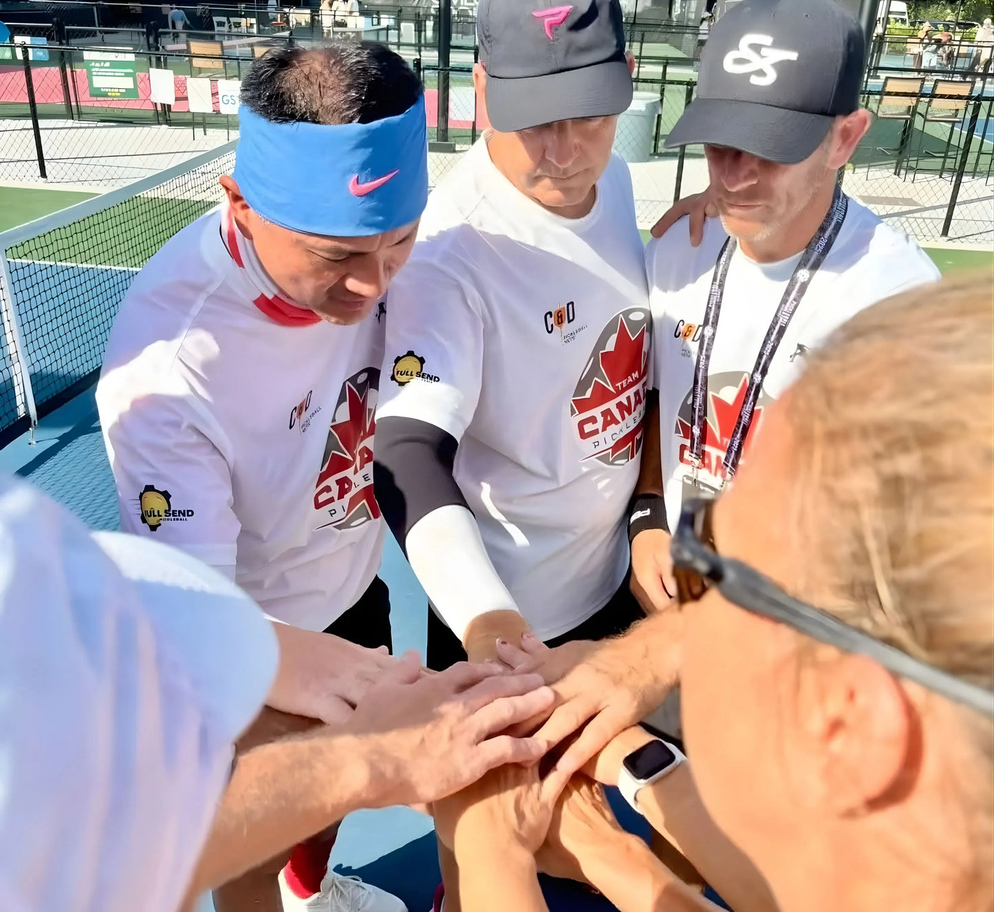 Three men in sports attire with visible branding on a pickleball court, interacting with a woman.